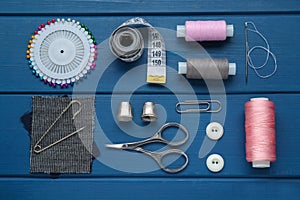 Flat lay composition with thimbles and different sewing tools on blue wooden table