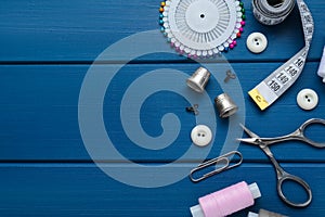 Flat lay composition with thimbles and different sewing tools on blue wooden table. Space for text