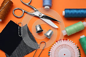 Flat lay composition with thimbles and different sewing tools on orange background