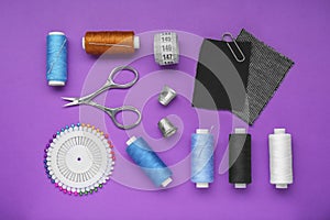 Flat lay composition with thimbles and different sewing tools on purple background