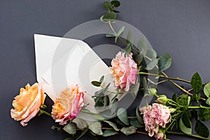 Flat lay composition with a white envelope, blank card and a peony rose flower on a grey background