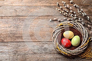 Flat lay composition of wicker nest with painted Easter eggs and willow on wooden table