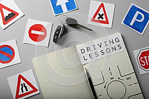 Flat lay composition with workbook for driving lessons and road signs on light grey background. Passing license exam photo