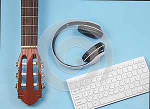 Flat lay of computer keyboard, headphones and acoustic guitar on blue background with copy space. Musician, leisure  and online