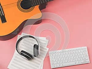 Flat lay of computer keyboard, headphones, blank music sheet and acoustic guitar on pink background. Music online learning and