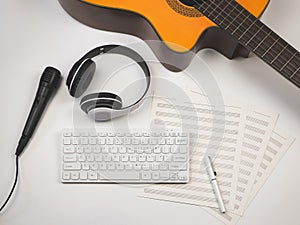 Flat lay of computer keyboard, headphones, microphone, blank music sheets and acoustic guitar on white background. Online music