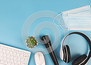 Flat lay of computer keyboard, mouse, microphone, headphones and medcal face masks on blue background. Online teaching or online