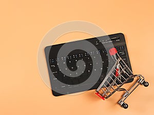 Flat lay of computer keyboard with shopping cart on orange background  with copy space. Shopping online concept