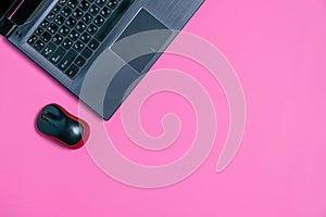Flat lay, computer mouse and laptop on a pink background, copy space