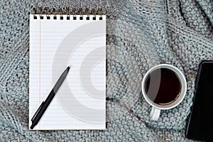 Flat-lay of Cosy working writing place with warm sweater coffee, note paper and smartphone. work from home. Writing