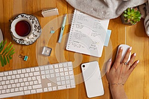 Flat lay of cozy workplace. Schedule planner, keyboard, phone and tea. Female hand holding mouse