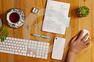 Flat lay of cozy workplace. Schedule planner, keyboard, phone and tea. Female hand holding mouse