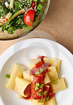 Flat lay. Cropped photo of a healthy vegan meal consisting of vegetarian herb salad and cooked italian pasta with tomato sauce and