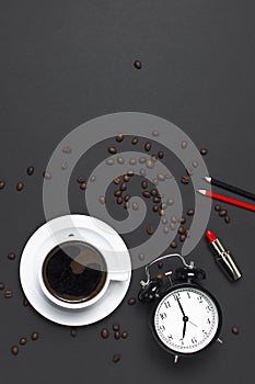 Flat lay cup black coffee, coffee beans, black alarm clock, red lipstick, color pencils on gray dark background top view