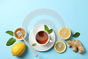 Flat lay. Cup of tea, lemon, ginger, mint, honey and dipper on blue background