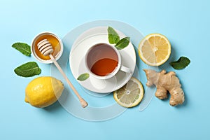 Flat lay. Cup of tea, lemon, ginger, mint, honey and dipper on blue background