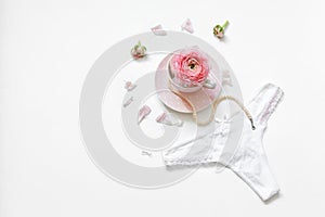 Flat lay a cup of tea with a string of pearls near flower petals and women`s thong on a white background. Place for text. Minimal