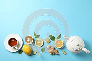 Flat lay. Cup of tea, teapot, lemon, ginger, mint, honey and dipper on blue background