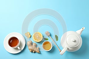 Flat lay. Cup of tea, teapot, lemon, ginger, mint, honey and dipper on blue background