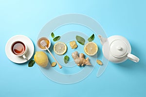 Flat lay. Cup of tea, teapot, lemon, ginger, mint, honey and dipper on blue background