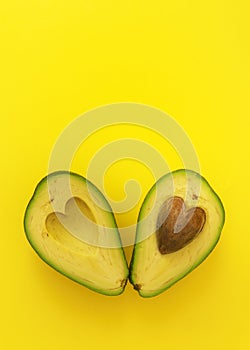 Flat lay of cut in half avocado with seed in shape of heart on yellow background love forever inseparable concept photo