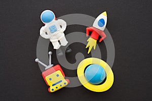 Flat lay of cute astronaut, rocket, robot and planet outer space eraser toy set on black background minimal style.