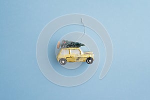 Flat lay of cute Christmas tree on yellow car toy with blue background copy space. Christmas composition ornament in holiday