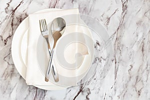Flat lay is cutlery, fork and knife on a napkin on an empty white plate on a marble table