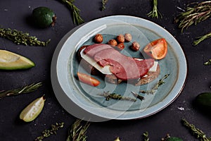 Flat lay of delicious bacon and cheese sandwich, tomatoes, hazelnuts, fruits and vegetables on black background, top view, closeup