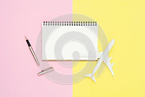 Top view mock up of blank white paper notebook, ball pen and airplane on pink and yellow pastel color screen.