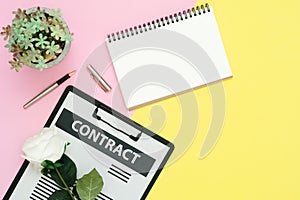 Flat lay design of working space - Top view mockup of contract document, pen and white paper notebook with rose and tree on pink