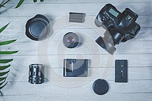 Flat lay with different photoaccessories on the table: camera, lenses, battery, charger, synchronizer, and lens covers