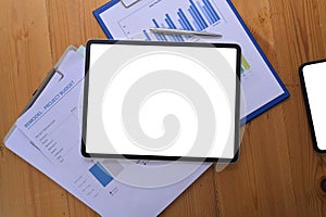 Digital tablet with white screen and financial documents on wooden desk.