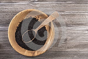 Flat lay of dried seeds of black cumin seeds kalinji on wooden plate with wooden spoon on rustic gray background