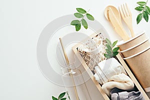 Flat lay eco-fiendly bags, paper cups, bamboo cutlery, galss water bottle with green leaves on white background