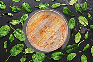 Flat lay empty wooden plate and fresh spinach leaves on a dark background. Top view