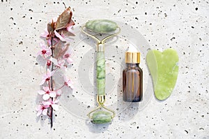 Flat lay with facial massage kit on stone concrete background - jade gua sha tool and face roller