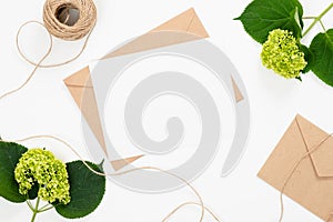 Flat lay fashion office desk. Female workspace with blank paper card, craft envelope, green flower bouquet on white background.