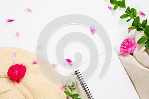 Flat lay fashion office desk. Female workspace with straw hat, blank paper notepad, pink rose flower buds and petal on white