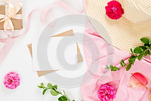 Flat lay fashion office table desk. Female workspace with blank paper card, craft envelope, straw hat, rose flower buds, gift box