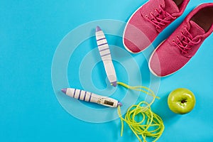 Flat lay of female sport equipments in pink color with jump rope and sneakers on blue background