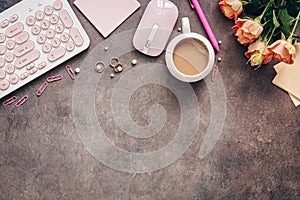 Flat lay female workspace - modern keyboard, mouse, cup of coffee, rose flowers, jewelry and stationery on a dark rustic