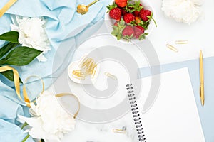 Flat lay feminine home office workspace with peony flowers, paper notepad and golden decorations on marble background. Top view