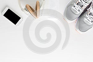 Flat lay of fitness accessories on white wooden background. Running shoes, towel, smartphone and headphone from top view.