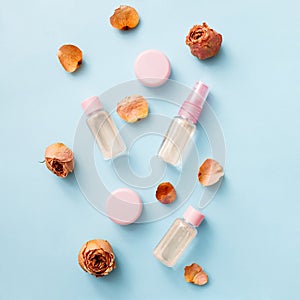 Flat lay of flowers and cosmetics products with Rose essential oil: toner, serum, essence, moisturizer and others on blue