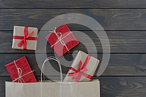 Flat lay of four gift boxes tired with ribbon, new year stuff look out from paper bag on wooden background, copyspace.