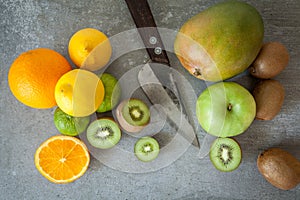 Flat lay of fresh citrus fruits, half cut kiwi orange and lemons on cutting board with knife on stone background.