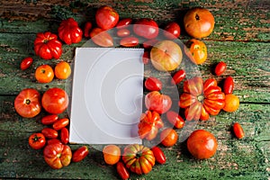 Flat-lay of fresh colorful ripe Fall or Summer heirloom tomatoes variety over rustic background with blank paper top