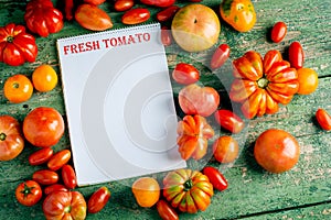 Flat-lay of fresh colorful ripe Fall or Summer heirloom tomatoes variety over rustic background with blank paper top