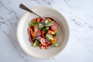 Flat-lay of a fresh colorful tomato salad in a white bowl, vegan, vegetarian food